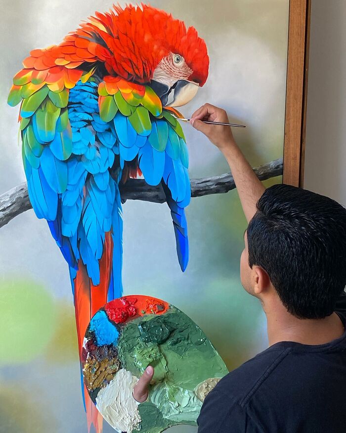 Brazilian artist painting vibrant feathers on a canvas with a palette in hand.