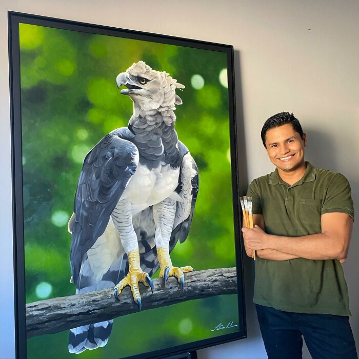 Brazilian artist with feather art painting of an eagle, smiling and holding brushes.