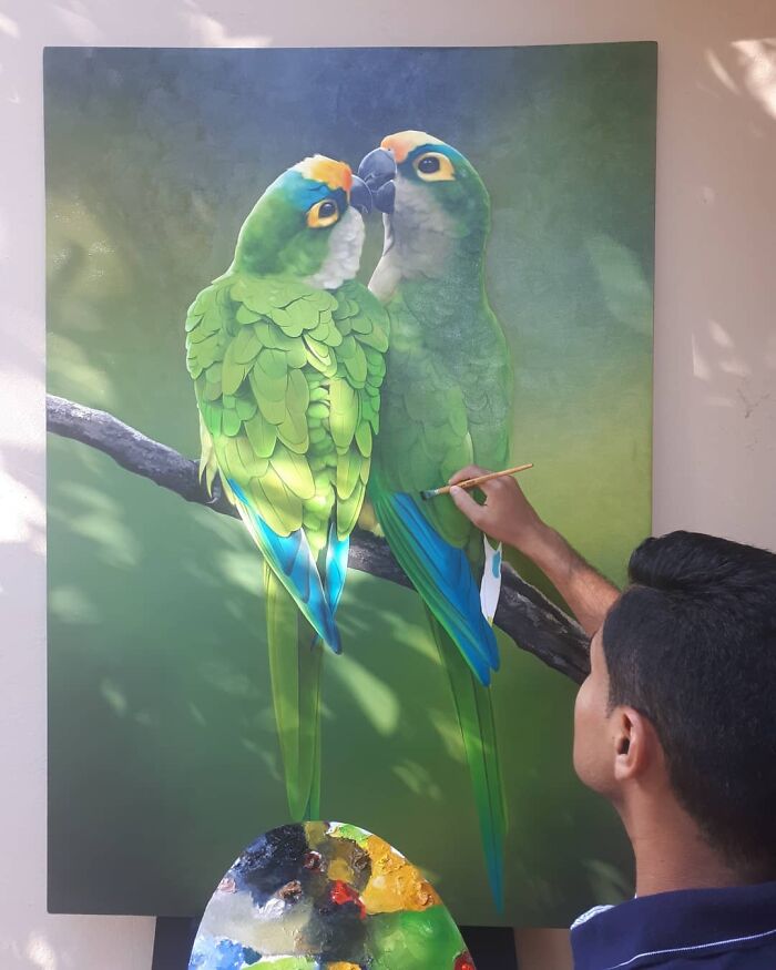 Brazilian artist painting vibrant parrots on canvas, showcasing feather art techniques.