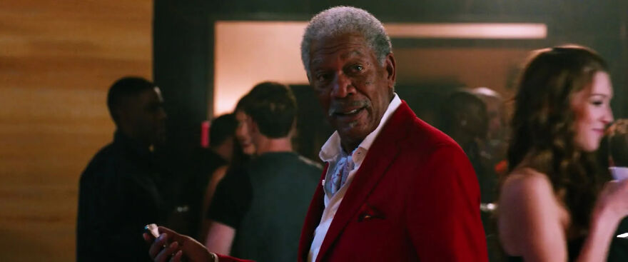 Actor Morgan Freeman in a red suit holding a drink at a party, surrounded by people, representing actors who always play themselves.