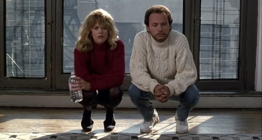 Couple sitting together on a wooden floor in front of large windows, reflecting on their relationship in the movie called When Harry Met Sally.