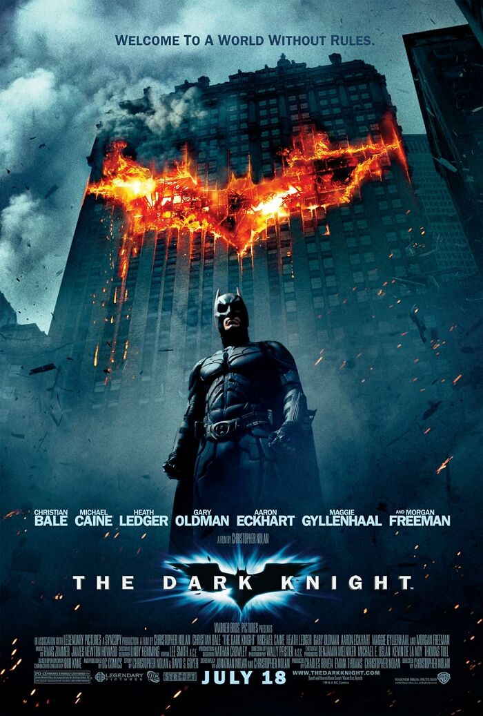 Batman stands before a burning building, representing IMDb's top movies and cinematic masterpieces.