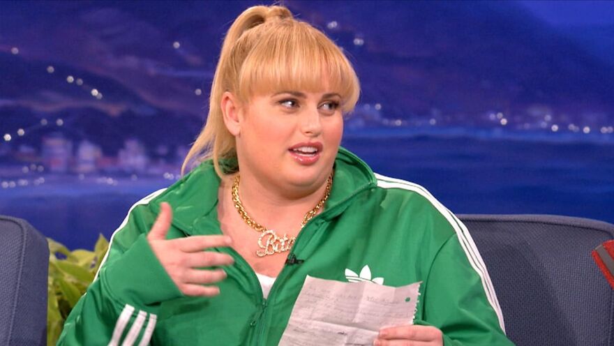 Actress Rebel Wilson wearing a green tracksuit, speaking on a talk show.