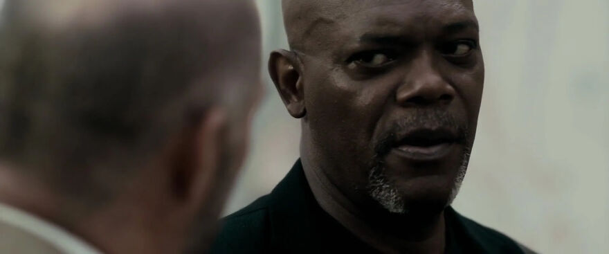 Bald man with a serious expression played by Samuel L. Jackson talking to another person, showcasing actors who play themselves in movies.