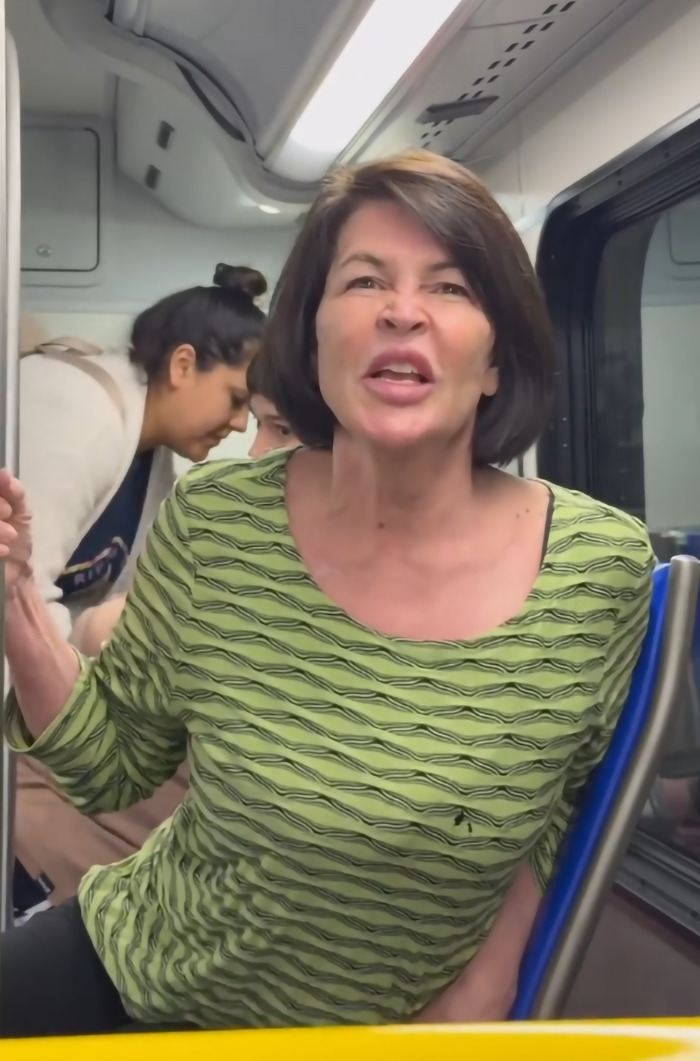 A woman in a green shirt on a bus, visibly upset, with other passengers in the background.