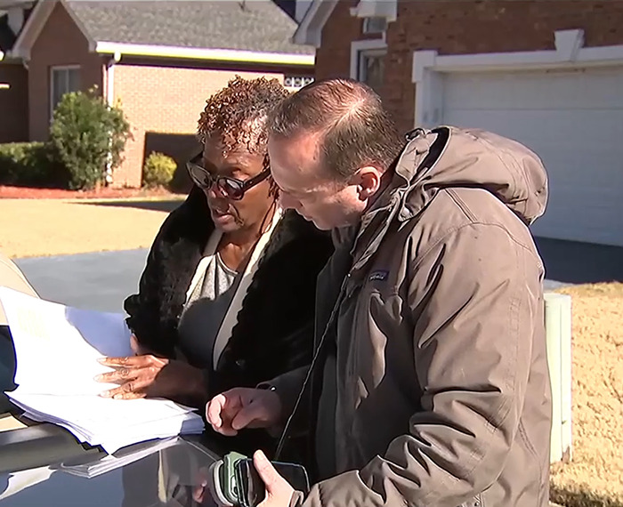 Loletha Hale reviewing documents outside her home with another person, related to squatter issue.