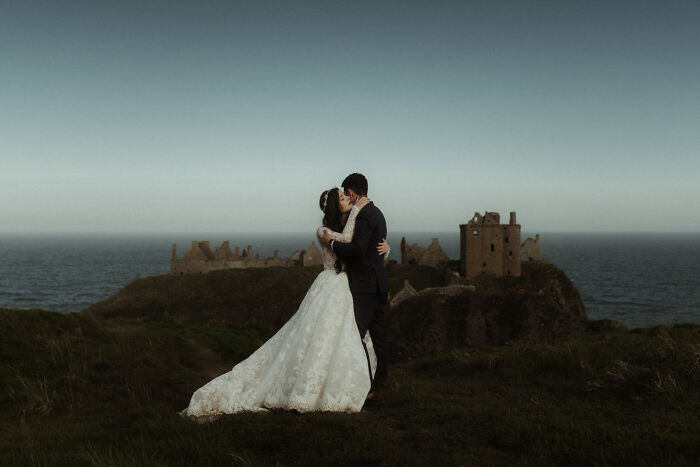 Bride and groom embrace on a cliff with a castle backdrop, showcasing top wedding photos of 2024.