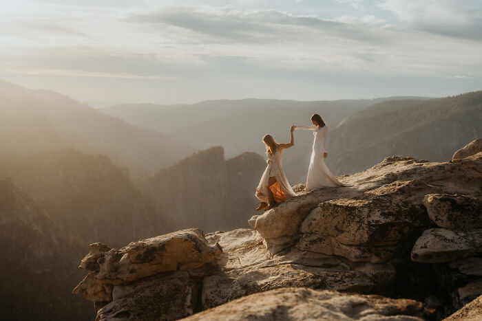 Brides in wedding dresses dancing on a mountain cliff with a scenic view in 2024.