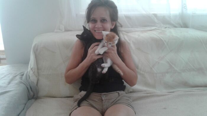 Smiling woman on a sofa holding two kittens at Romania’s largest cat sanctuary.