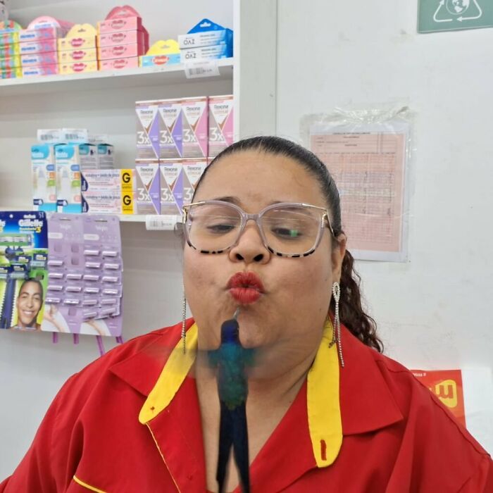 Woman in store wearing glasses and red uniform, interacting with a hummingbird, capturing a magical moment in Brazil.