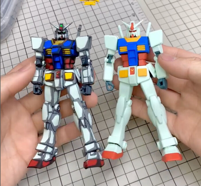 Gundam action figures, one painted with detailed enhancements, held in hand for a before-and-after comparison.