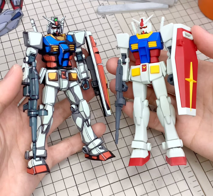 Two Gundam action figures, one painted with detailed upgrades and the other unpainted, held in hands.