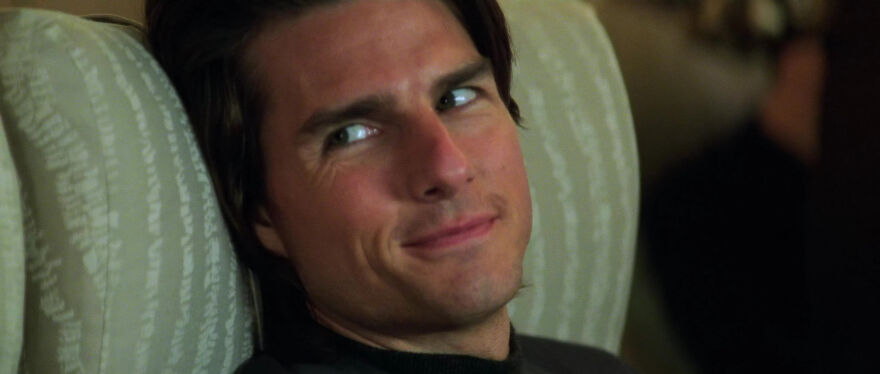 Actor Tom Cruise with a confident smile reclining in a chair, embodying a familiar persona onscreen.