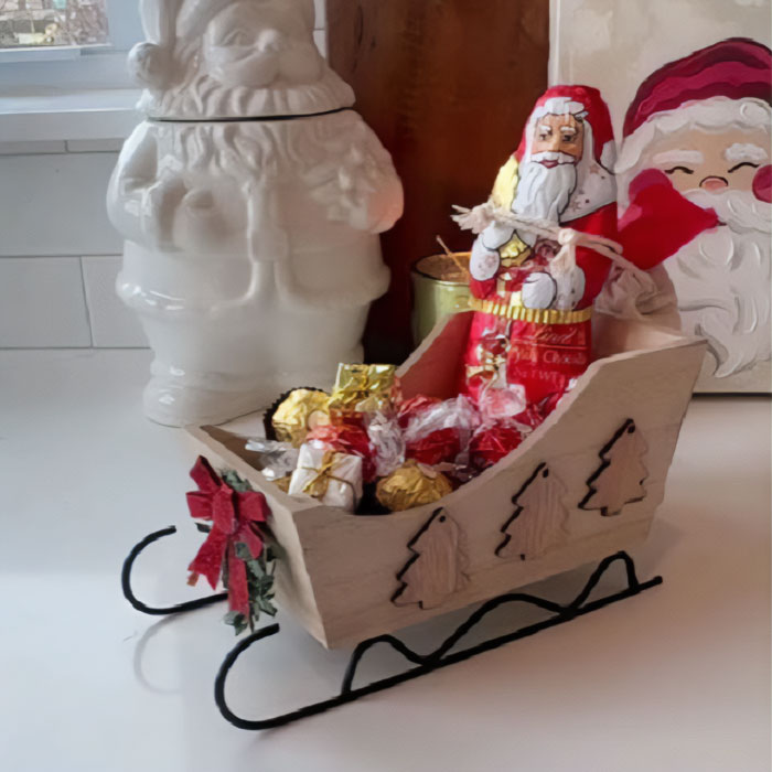 Red sleigh filled with gold gift boxes and ornaments, a creative way to present a gift card.