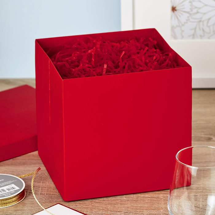 Red gift box with shredded paper, a creative way to present a gift card, placed on a wooden table.