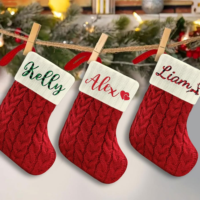 Red knitted Christmas stockings labeled Kelly, Alex, and Liam, hanging on a festive garland, perfect for gifting a gift card.