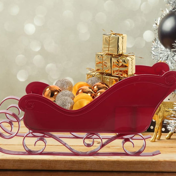 Red sleigh filled with gold gift boxes and ornaments, a creative way to present a gift card.