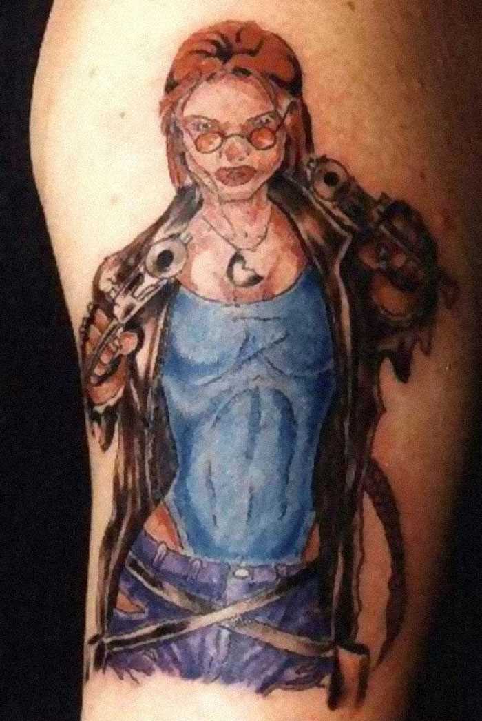 Humorous tattoo fail depicting a stylized figure with glasses, holding guns, in a blue shirt and brown jacket.