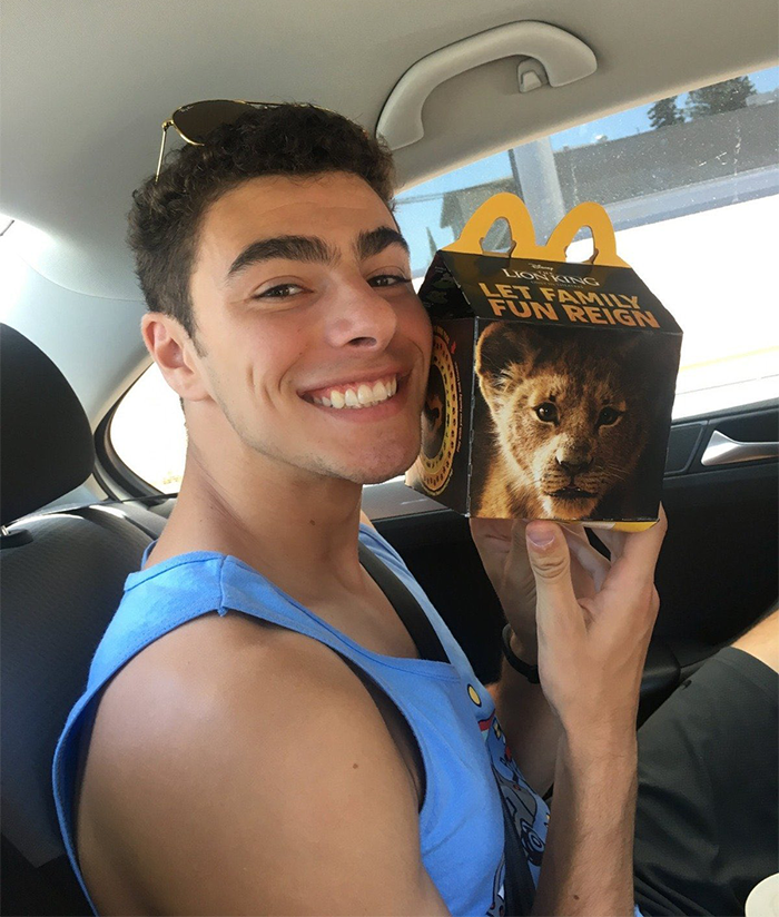 Luigi Mangione smiling with McDonald's Happy Meal box in a car.