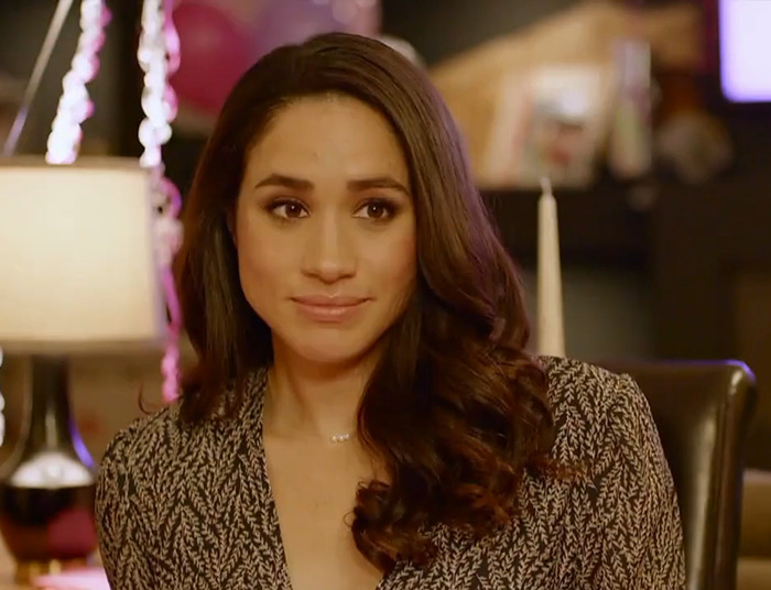 Meghan Markle in a living room, seated with a subtle smile, wearing a patterned blouse.