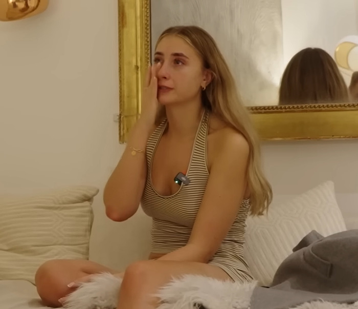 Model Lily Phillips in emotional breakdown, sitting on a bed and wiping tears from her eyes.