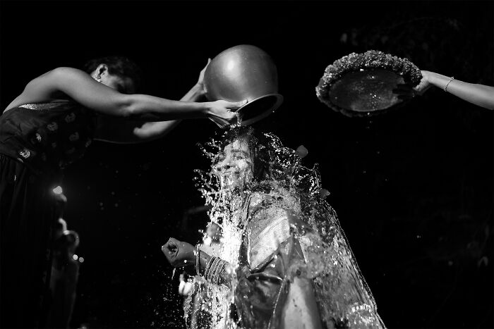 A bride in a traditional ceremony, smiling while water is poured over her, featured in top wedding photos of 2024.