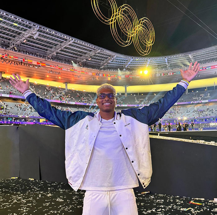 French Olympian celebrating under illuminated rings at Paris 2024 stadium.