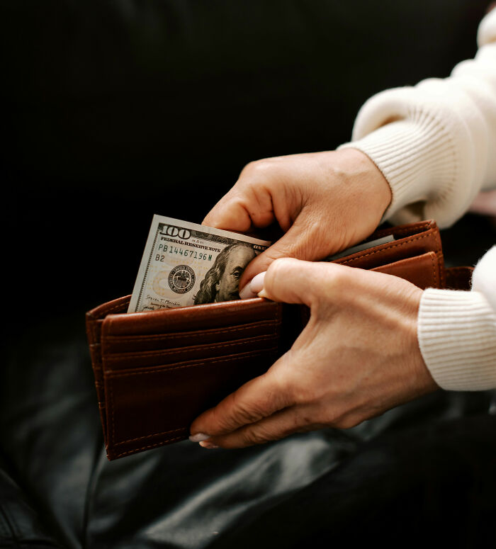 Rich kid holding a hundred dollar bill in a wallet, displaying wealth.