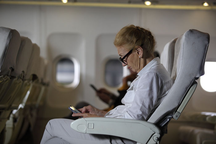 Elderly woman in plane seat using phone, with mobility keywords highlighted in context.