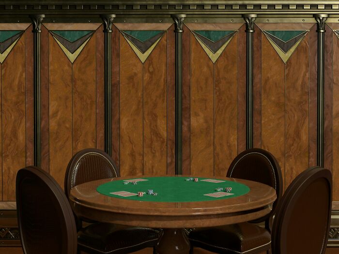 Poker table in casino setting, empty chairs around a felt table with cards and chips placed on it.