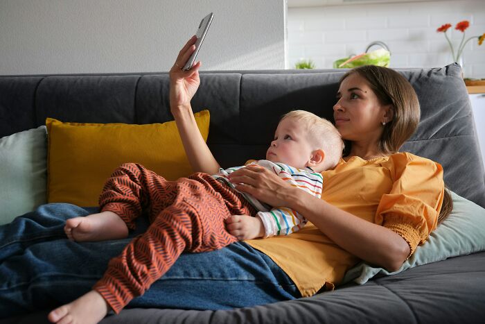 A woman and child on a sofa looking at a phone, engaging in a moment of judgment-free relaxation.