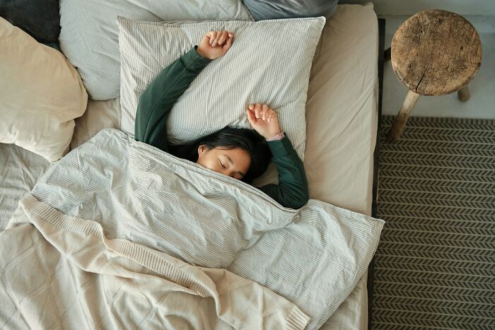 Person sleeping in bed with simple bedding, highlighting habits influenced by poverty on a minimalist wooden bedside table.