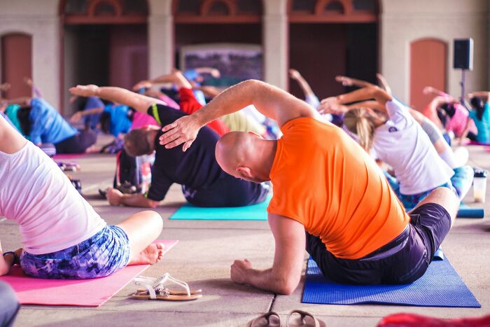 People in a group exercise class performing stretches on yoga mats indoors.