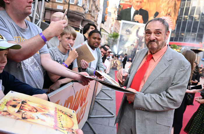 Actor in a gray suit signing autographs, surrounded by fans on the red carpet, related to Aquaman 2 cast event.