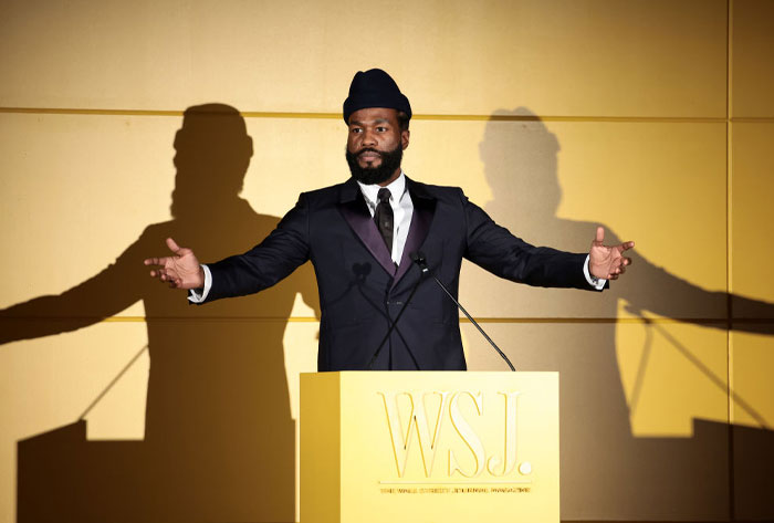 Man in a suit at a WSJ event, gesturing with arms wide open.