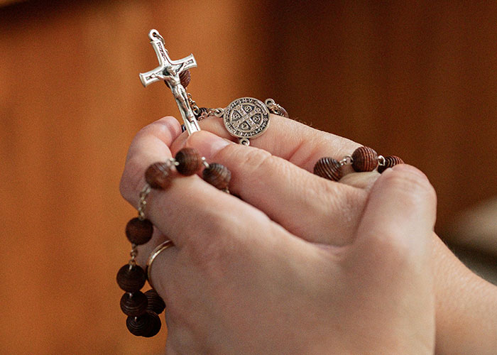 Hands holding a rosary, symbolizing contemplation or prayer, related to a wedding date change.