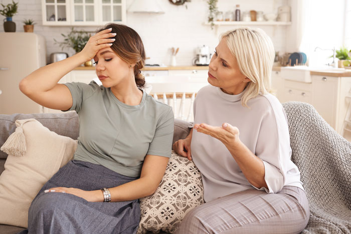 Aunt-in-law discussing with a frustrated new mom on a couch, highlighting family tension.