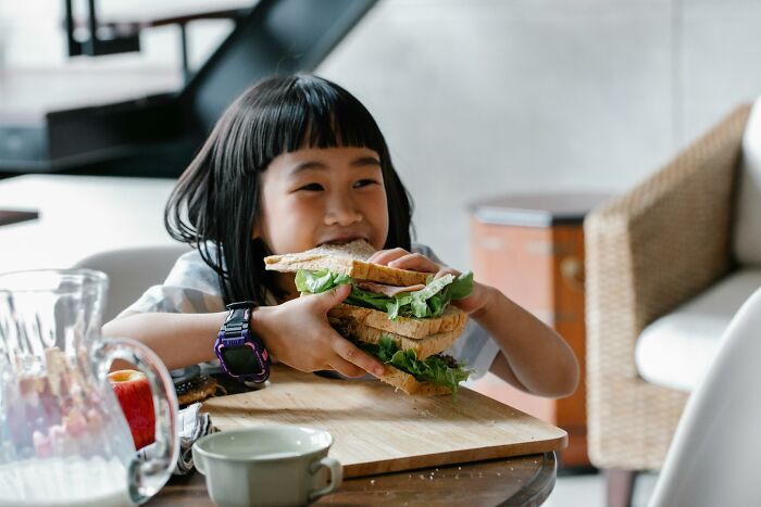 Child smiling while holding a large sandwich, embodying babysitters' insights on unique childhood experiences.