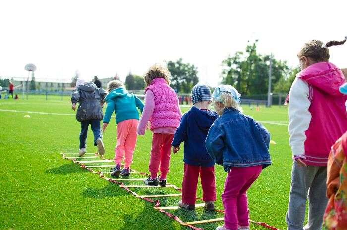 Children playing outside in a park, balancing on a ladder, wearing colorful jackets and pants.