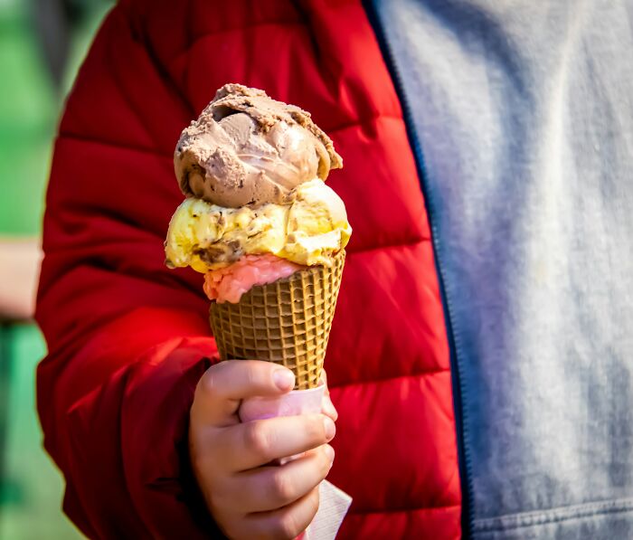 Child holding a triple-scoop ice cream in a red jacket, symbolizing carefree childhood moments.