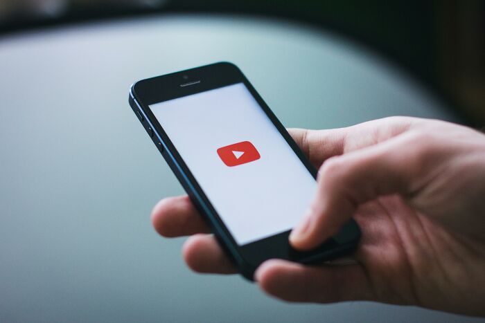 Hand holding a smartphone with the YouTube logo, related to babysitters' stories about unconventional childhoods.