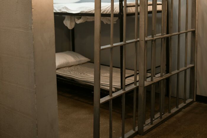 Bunk beds in a dimly lit room with metal bars, conveying a sense of confinement.