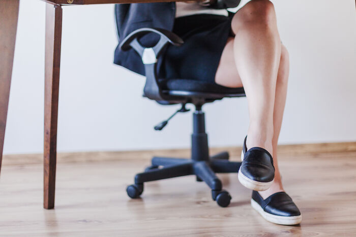 Person sitting on an office chair with crossed legs, showing relaxed posture; concept of bad-good-habit.