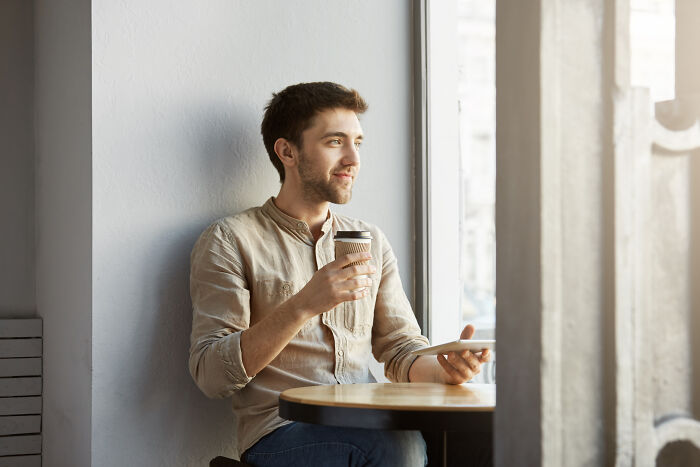 Man enjoying coffee at a café window, reflecting on bad-good-habit changes.