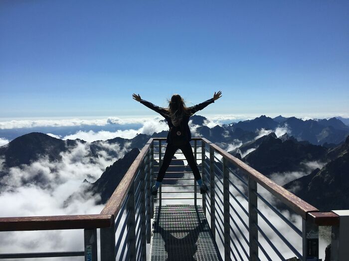 Person stands on mountain overlook, arms outstretched in the sky, representing freedom and breaking bad-good-habit.