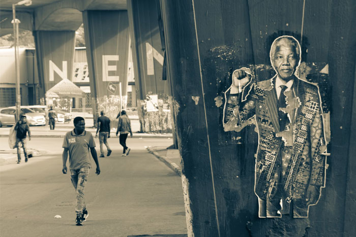 Street art of a man in a suit on a pillar, with pedestrians walking under a bridge.