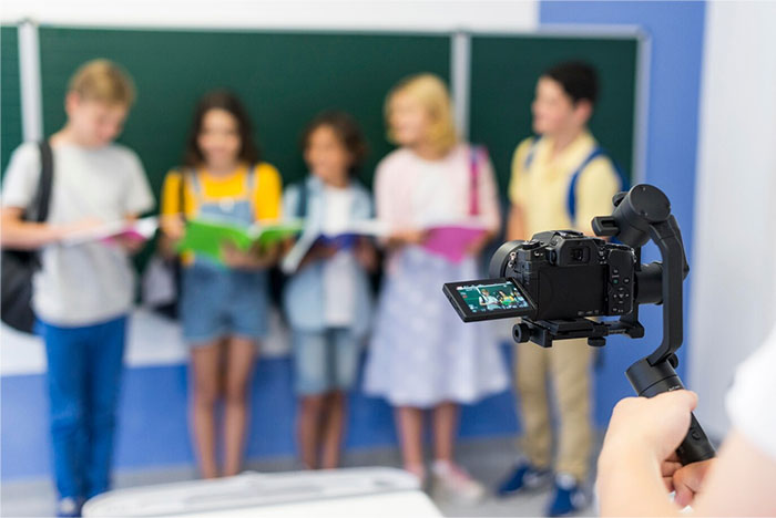 Students with books in front of a blackboard being filmed, showcasing a school presentation.