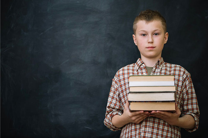 "A boy in a plaid shirt holding books in front of a chalkboard, representing school presentations."