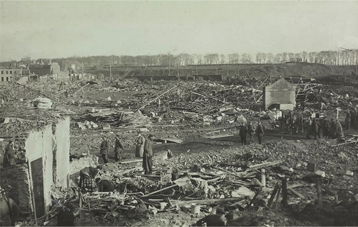 An old photo showing people walking through a vast, barren landscape scattered with debris and ruins.