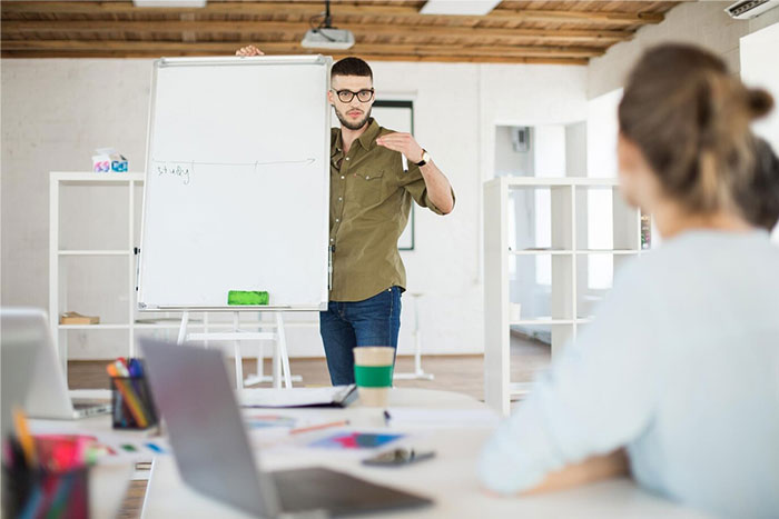 Person giving an unengaging school presentation, standing next to a whiteboard in a classroom setting.